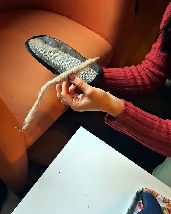 Gant Câlin bleu tenu devant un fauteuil orange, avec un cordon de poils ramassés posé dessus